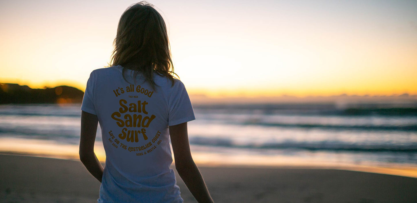 A woman looks out to the surf of a beautiful Australian beach at sunrise, wearing a cotton t shirt