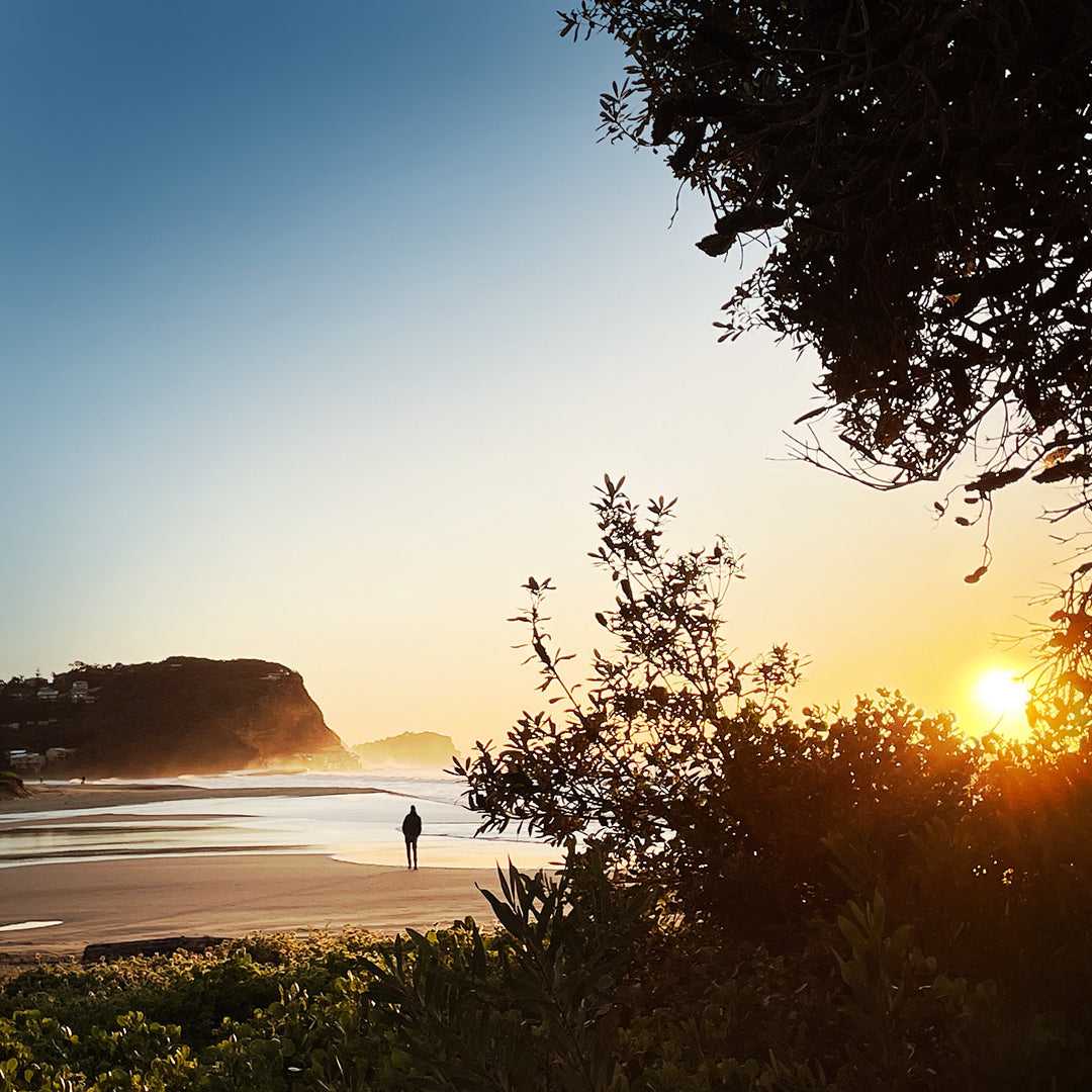 The sun rises on North Avoca Beach as a single figure walks along the beach