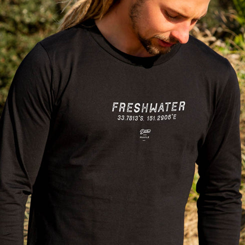 Men’s Long Sleeve Cotton T Shirt with Freshwater Beach graphic design, Black, Front, close up on male model