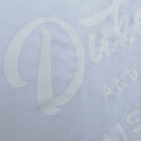 Close up of The Flat White, white vinyl D&H logo on a white 100% cotton long sleeve unisex fit tee